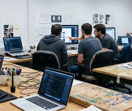 Design studio with creative tools spread across a shared workroom: laptops, drawing tablets, marker cups